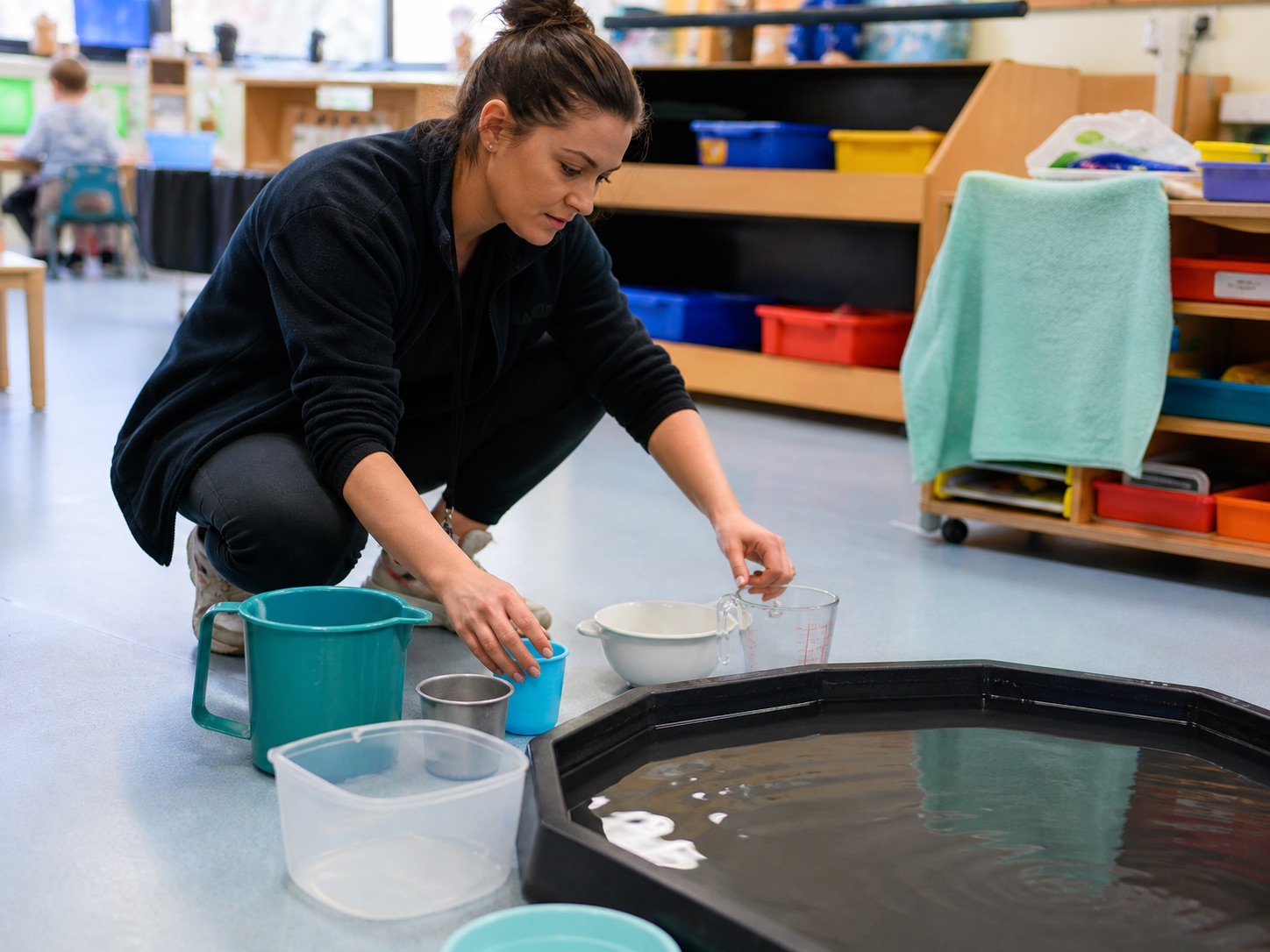 A practitioner arranging containers of different sizes beside a water tray, setting up the next activity